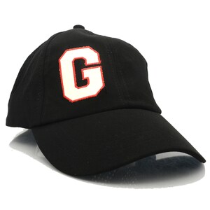 May include: Black baseball cap with a white letter "G" embroidered on the front. The letter is outlined in red.