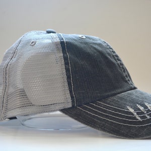 May include: A gray and white trucker hat with a mesh back. The hat has a distressed look and a curved brim.