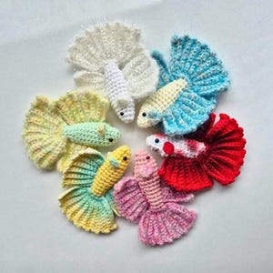 Op de afbeelding: Zes gehaakte betta-vissen in een cirkel gerangschikt. De vissen zijn in verschillende kleuren, waaronder wit, lichtblauw, groen, geel, roze en rood.