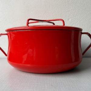 Può includere: Una pentola in smalto rosso vivo con coperchio abbinato. La pentola ha due manici laterali e un manico sul coperchio. L'utensile da cucina è di colore rosso brillante, perfetto per cucinare e servire.