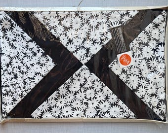 May include: A packaged textile item featuring a black and white floral pattern. The design is arranged in a geometric layout with diagonal black stripes. A tag with the word "Vera" is visible.