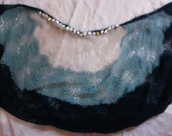 May include: A teal and black knitted shawl with a white beaded trim. The shawl is made of a soft, fuzzy yarn.