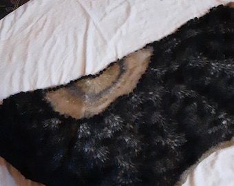 May include: A black and white knitted shawl with a scalloped edge. The shawl is made of a soft, fuzzy yarn and has a delicate, lacy pattern.