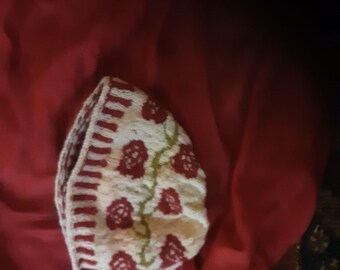 May include: A white and red knitted hat with a floral pattern. The hat has a red and white striped band around the bottom.