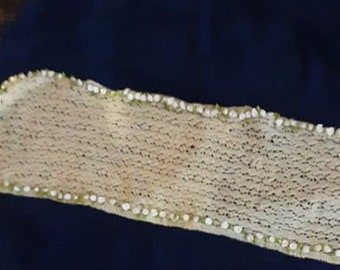 May include: A navy blue textile with a cream-colored, open-weave strip across the center. The strip is edged with small white and green beads. The fabric appears to be folded or draped.
