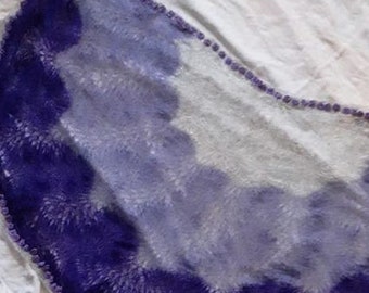 May include: A purple and white knitted shawl with a scalloped edge. The shawl is made of a soft, fuzzy yarn and has a gradient of color from dark purple to white.
