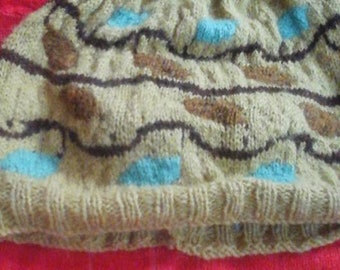 May include: A beige knitted hat with a brown and blue geometric pattern. The hat is folded in half and lying on a red surface.