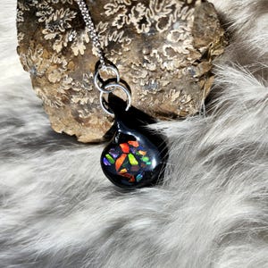 May include: A black teardrop-shaped pendant necklace with a colorful stained glass design. The pendant is hanging from a silver chain.