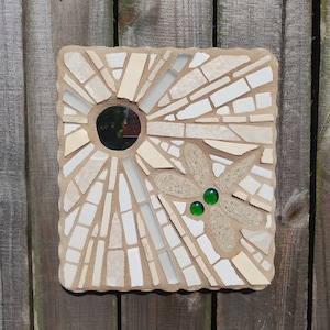 May include: A white mosaic tile with a round mirror in the center and a stylized flower design with green glass accents.