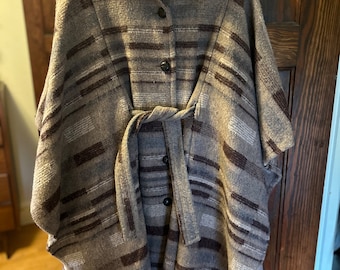 May include: A brown and gray striped wool cape with a button closure and a tie belt. The cape has a collar and is lined with a brown fabric.