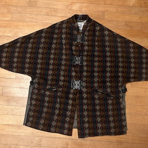 May include: A brown, black, and beige patterned cape with a high collar and three black buckles down the front.