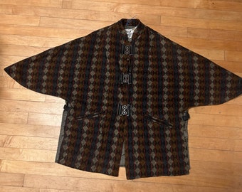 May include: A brown, black, and beige patterned cape with a high collar and three black buckles down the front.