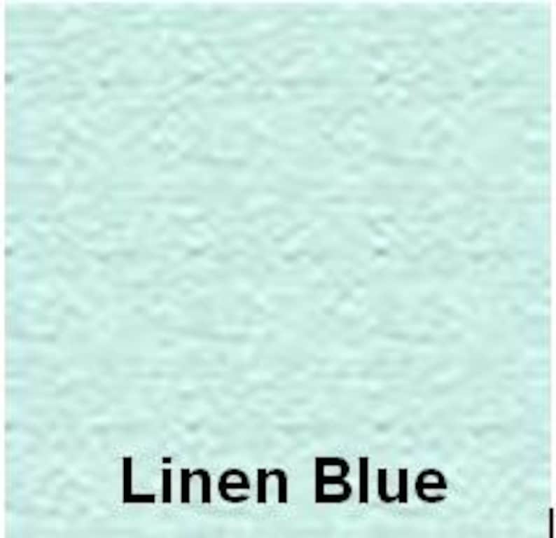 Op de afbeelding: Een effen, licht pastelblauw vierkant kleurstaal met een zichtbaar, fijnkorrelig, getextureerd oppervlak. De tekst "Linen Blue" is in een vet, zwart, schreefloos lettertype onderaan in het midden van de afbeelding gedrukt.
