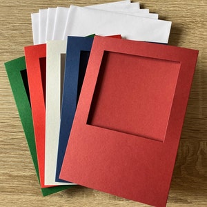Op de afbeelding: Een verzameling gekleurde passe-partouts in verschillende tinten, waaronder rood, groen, blauw en wit. Elk passe-partout heeft een rechthoekige opening en ze zijn op elkaar gestapeld. De passe-partouts zijn gemaakt van dik papier of karton.