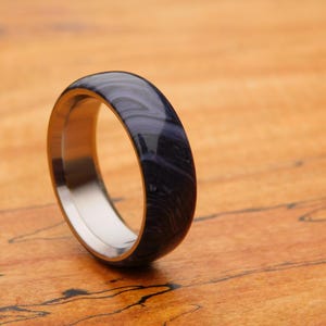 May include: A dark blue and silver ring with a swirling pattern. The ring is made of titanium and has a polished finish.