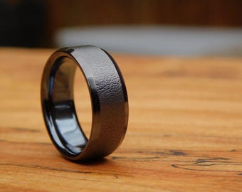May include: A black ring with a textured finish. The ring is made of a durable metal and has a polished edge.