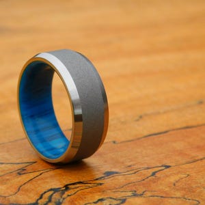 May include: A gray and blue ring with a brushed metal finish. The ring has a wide band with a blue inlay.