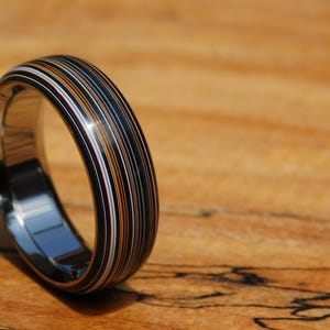 May include: A black ring with a multi-coloured inlay of thin stripes in shades of white, brown, and black.