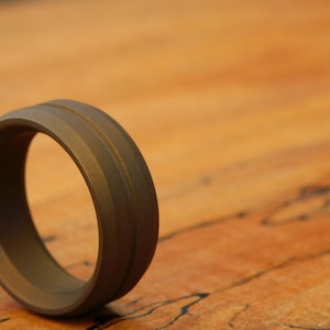 May include: A dark brown metal ring with two grooves running around the band.
