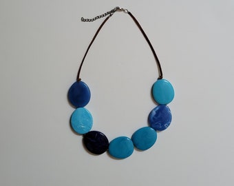 May include: A blue and turquoise necklace with a brown leather cord and a silver clasp. The necklace is made of large, round, flat beads.