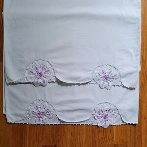Puede incluir: Dos fundas de almohada de algod&oacute;n blanco con delicado encaje floral morado. El encaje tiene un patr&oacute;n de fest&oacute;n.