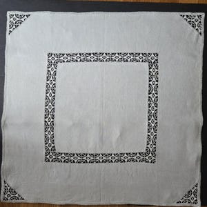 May include: A white linen tablecloth with a delicate black lace border. The lace design features intricate floral patterns.