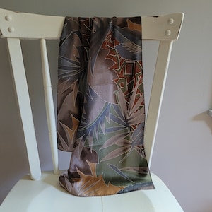 May include: A brown, green, and gold patterned silk scarf draped over a white wooden chair.