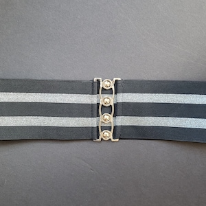 May include: Black elastic belt with two silver stripes and a silver buckle with four round metal accents.