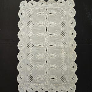May include: A white, rectangular doily with intricate cutwork and a scalloped edge. The design features floral and geometric patterns, creating a delicate and elegant aesthetic. The doily is made of a fine, sheer fabric.