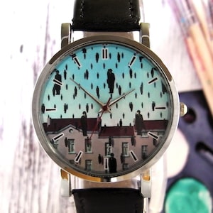 May include: A silver wristwatch with a black leather band. The watch face features a blue and white background with a black and white image of people walking on a rooftop. The watch face also has black Roman numeral hour markers.