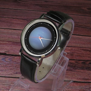 May include: A silver wristwatch with a black leather strap. The watch face has a black background with a blue and white circular design.