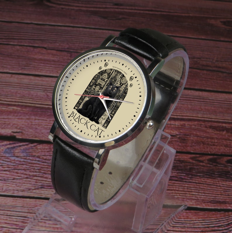 May include: A black leather wristwatch with a silver case. The watch face is cream colored with a black cat illustration and the text "BLACK CAT".