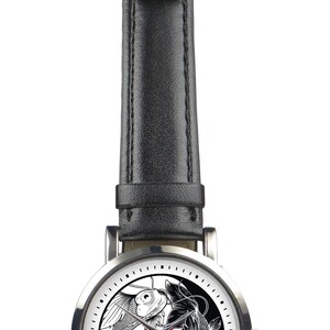 May include: A silver wristwatch with a black leather band. The watch face features a yin yang design with two black and white fish.