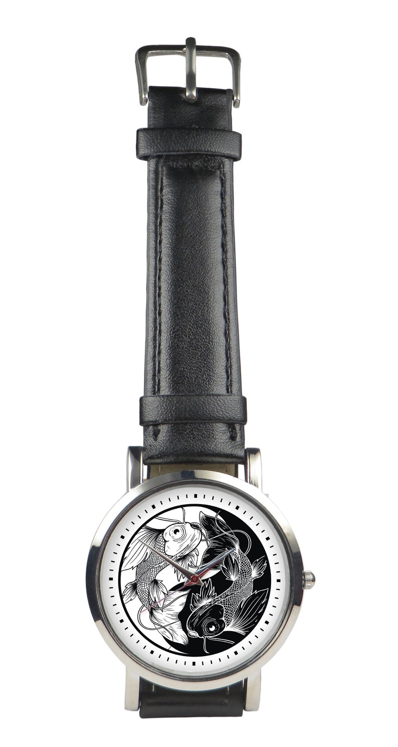 May include: A silver wristwatch with a black leather band. The watch face features a yin yang design with two black and white fish.