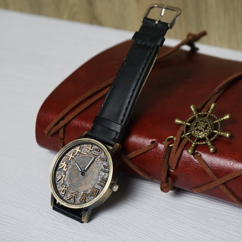 May include: A vintage-style wristwatch with a black leather band and a round, bronze-colored face. The face has Roman numerals and Chinese characters around the edge.