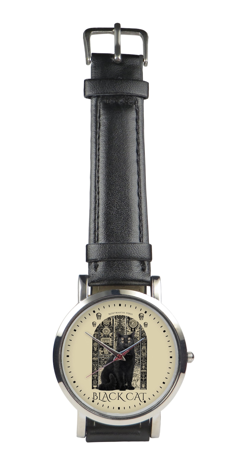 May include: A silver wristwatch with a black leather band. The watch face has a cream background with a black cat sitting in front of a detailed archway. The text "BLACK CAT" is printed below the cat. The text "MONTMARTRE PARIS" is printed above the archway.