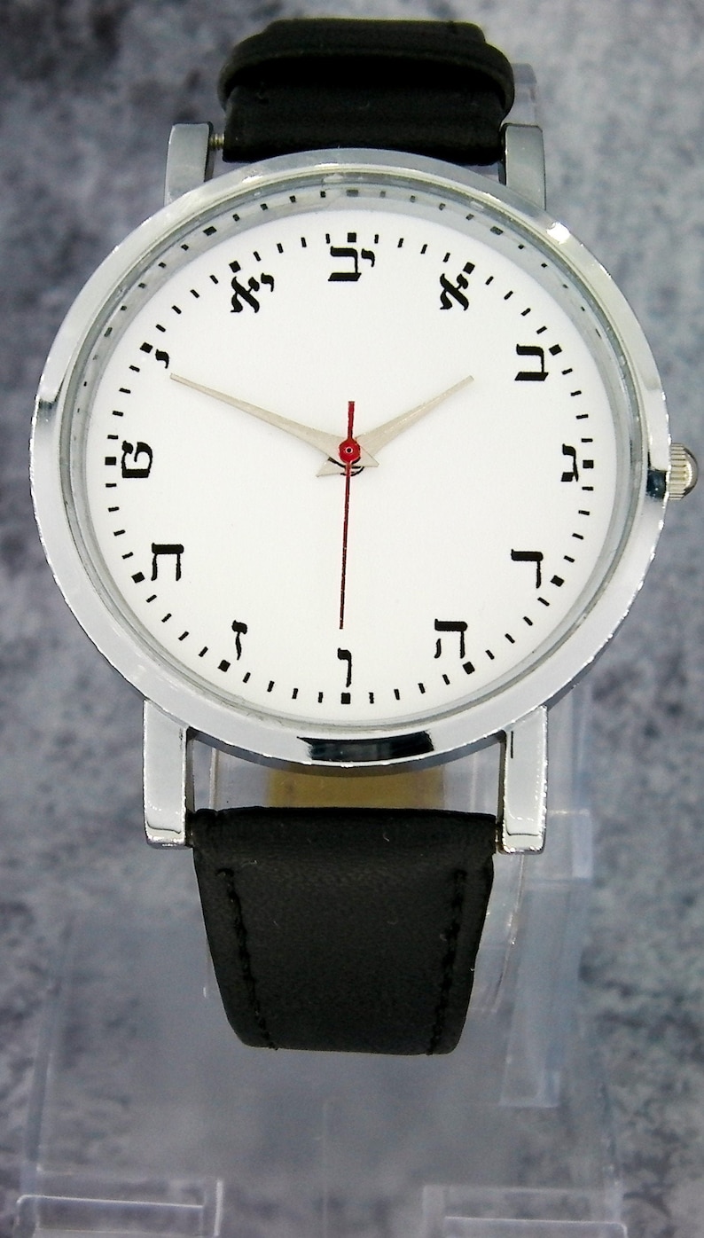 May include: A silver wristwatch with a white face and black leather band. The watch face has Hebrew numerals for the hours.