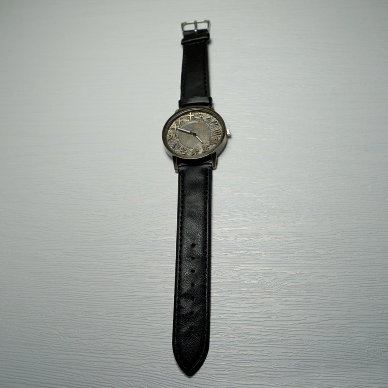 May include: A black leather wristwatch with a round, silver-toned face. The face has black Roman numeral markings and a black second hand.
