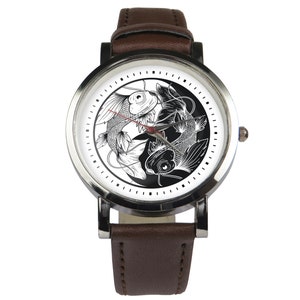 May include: A brown leather wristwatch with a silver face and a black and white yin yang design featuring two fish. The watch face has black markings for the hours and minutes.