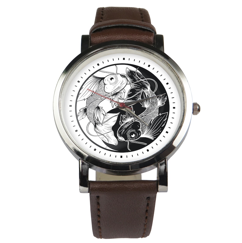 May include: A brown leather wristwatch with a silver face and a black and white yin yang design featuring two fish. The watch face has black markings for the hours and minutes.