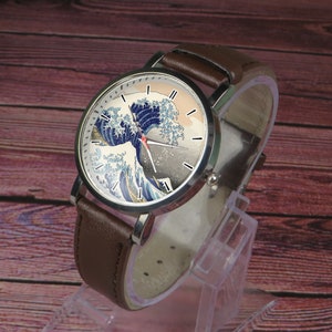 May include: A brown leather wristwatch with a silver case and a white face. The face features a colorful image of a wave, reminiscent of the Great Wave off Kanagawa by Hokusai.