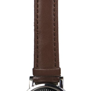 May include: A silver wristwatch with a brown leather strap. The watch face has a black background with a white circle in the centre. The circle has a blue and white design inside.