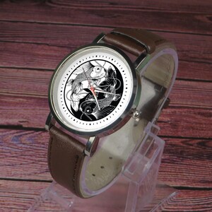May include: A brown leather wristwatch with a silver face and black and white yin yang design featuring two fish.