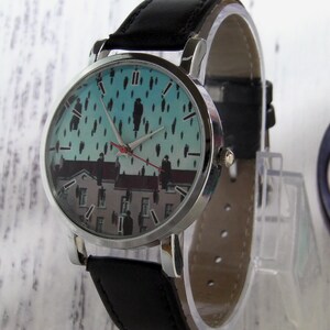 May include: A silver wristwatch with a black leather band. The watch face features a colorful image of people on a rooftop in the rain.