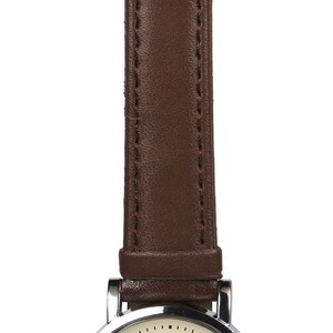 May include: A silver wristwatch with a brown leather band. The watch face features a black cat sitting in a doorway with a skull design. The text "BLACK CAT" is printed below the cat. The text "MONTMARTE PARIS" is printed above the cat.