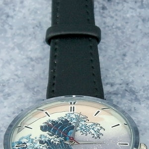 May include: A silver wristwatch with a black leather band and a face featuring a colorful image of a wave. The watch face has silver hands and Roman numeral hour markers.