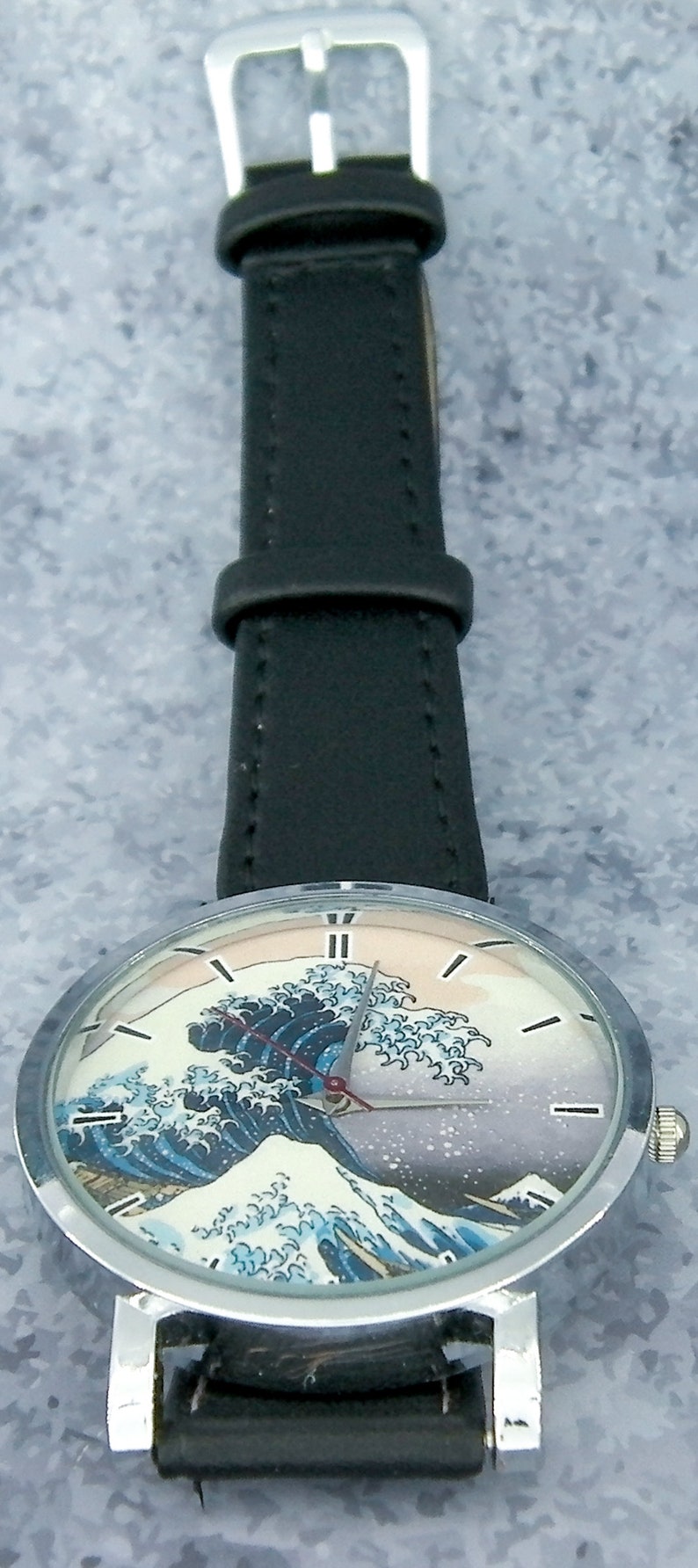 May include: A silver wristwatch with a black leather band and a face featuring a colorful image of a wave. The watch face has silver hands and Roman numeral hour markers.