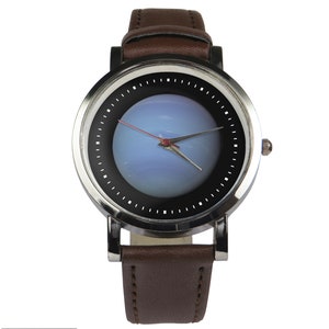 May include: A silver wristwatch with a brown leather strap. The watch face has a black background with a blue and white image in the centre. The watch hands are red and silver.