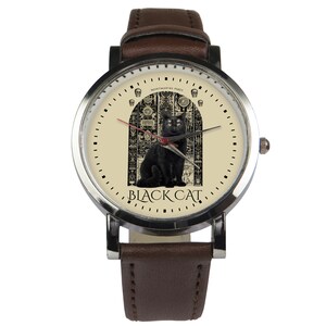 May include: A brown leather wristwatch with a silver face. The face features a black cat sitting in front of a detailed, ornate doorway. The text "BLACK CAT" is printed below the cat. The text "MONTMARTRE PARIS" is printed above the cat.