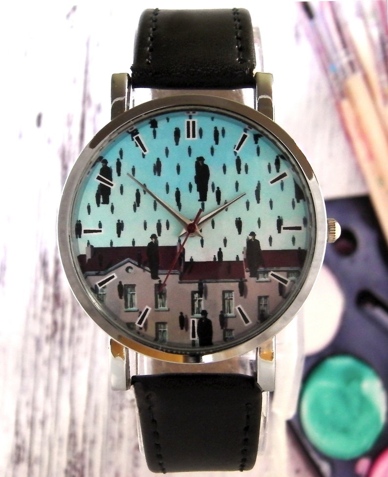 May include: A silver wristwatch with a black leather band. The watch face features a blue and white background with a black and white image of people walking on a rooftop. The watch face also has black Roman numeral hour markers.